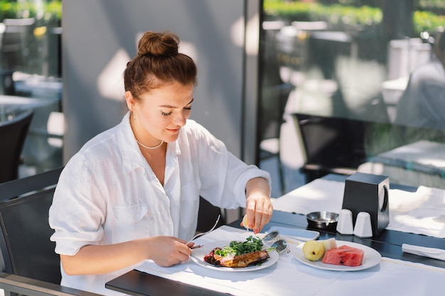 Een vrouw in een wit hemd eet lunch of ontbijt buiten in een café