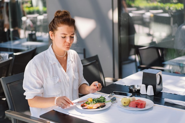 Een vrouw in een wit hemd eet lunch of ontbijt buiten in een café