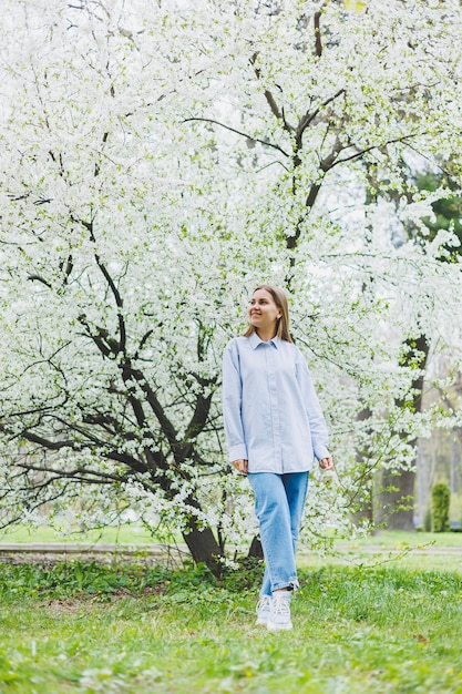 Een vrouw in een wit overhemd en een spijkerbroek met een bril in haar handen in een lentetuin