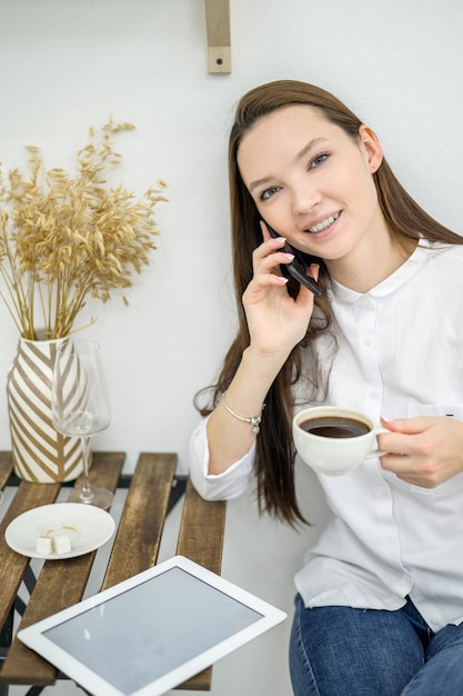 Een vrouw in een wit overhemd en spijkerbroek zit in een café en drinkt koffie Vrouwelijke kantoormedewerker tijdens de lunchpauze praten aan de telefoon Manager tijdens een zakelijke bijeenkomst in een restaurant