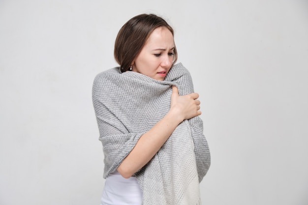Een vrouw in een wit shirt droeg een sjaal van de kou en koude rillingen. Verkoudheid en griep concept.