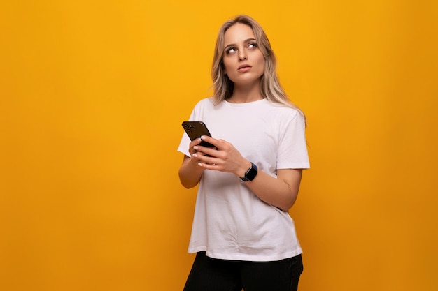 Een vrouw in een wit t-shirt met een smartphone in haar handen gebruikt een applicatie op een gele achtergrond