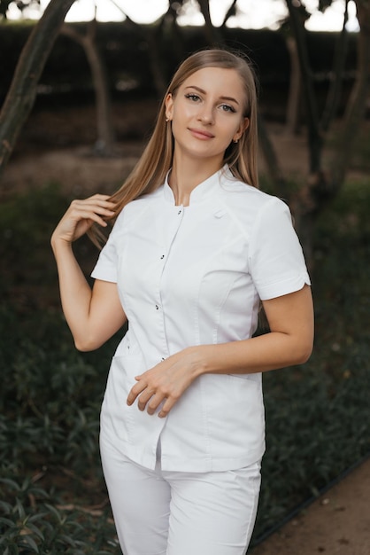 Een vrouw in een wit uniform staat voor een boom en draagt een wit topje