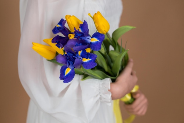 Een vrouw in een witte jurk houdt een boeket tulpen en irissen vast close-up 8 maart Vrouwendag Vrouwenvakantie Mama's vakantie Boeket bloemen