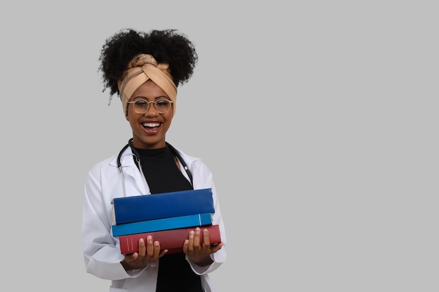 Een vrouw in een witte laboratoriumjas houdt boeken vast en glimlacht.