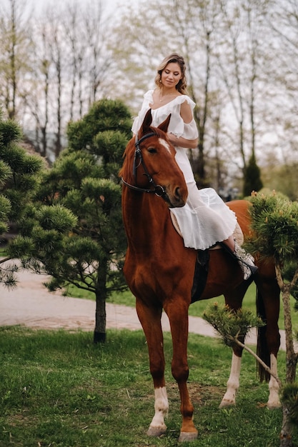 Een vrouw in een witte zomerjurk die op een paard rijdt in de buurt van een boerderij