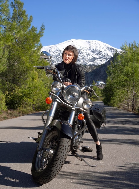 Een vrouw in een zwart leren bikerjack op een helikoptermotorfiets in Griekenland op een weg in het bos