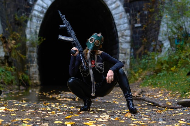 Een vrouw in een zwart pak en gasmasker met een machinegeweer in haar handen.