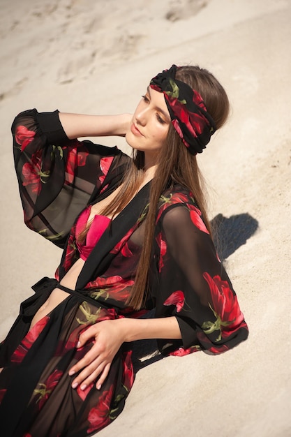 Een vrouw in een zwarte en rode kimono zit op het strand.