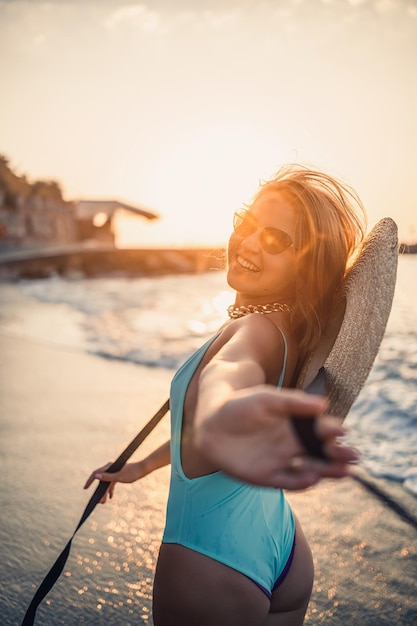 Een vrouw in een zwempak en een hoed met een bril loopt langs het strand bij zonsondergang Het concept van zeerecreatie Selectieve focus