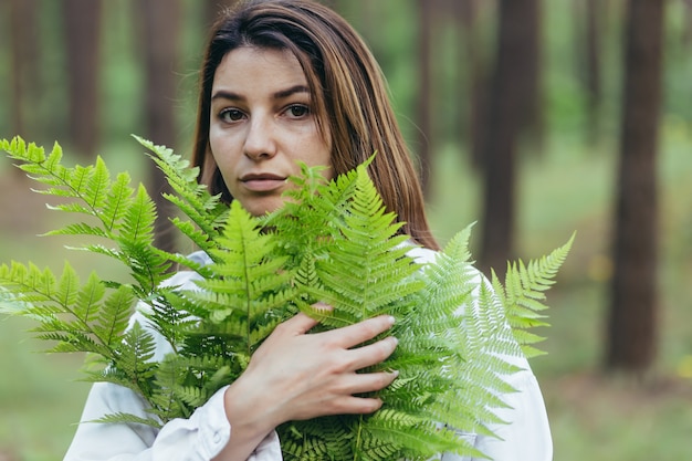 Een vrouw in het bos knuffelt een boeket varens, een jonge activist beschermt het bos