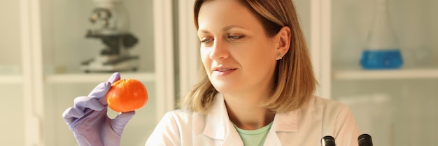 Een vrouw in het laboratorium kijkt naar een sinaasappelcitrusvrucht een close-up productie van biologische olie