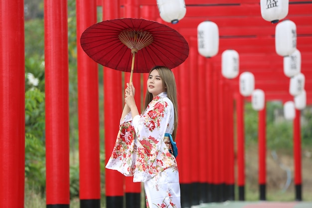 een vrouw in kimono met paraplu die het heiligdom binnenloopt, in Japanse tuin.