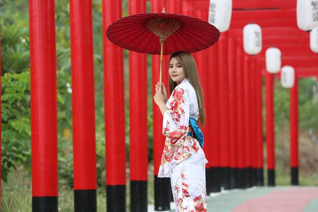 een vrouw in kimono met paraplu die het heiligdom binnenloopt, in Japanse tuin.