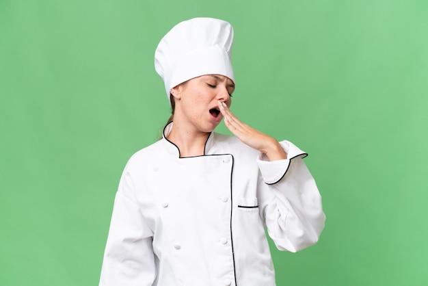 Een vrouw in koksuniform staat te geeuwen en heeft een groen scherm achter zich.