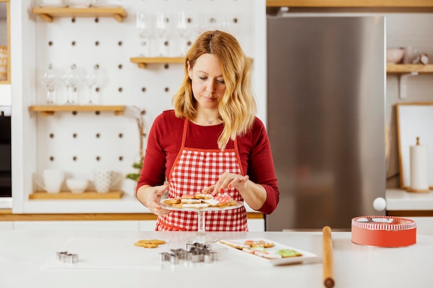 Een vrouw in schort regelt gemberkoekjes op een bord terwijl ze in de keuken staat