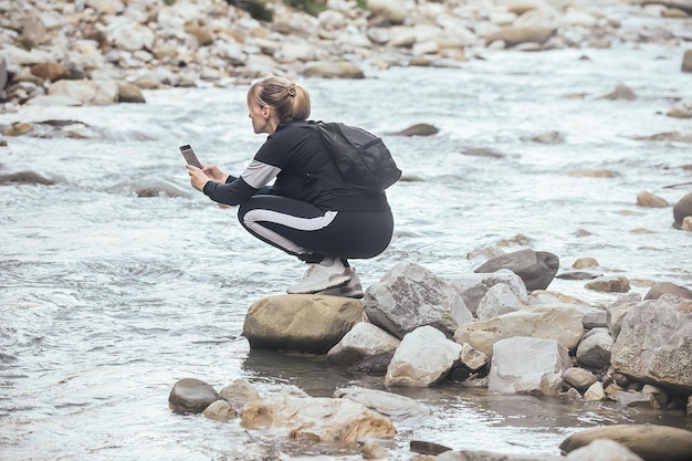 Een vrouw in sportkleding en met een rugzak maakt foto's van de natuur in de bergen aan de telefoon