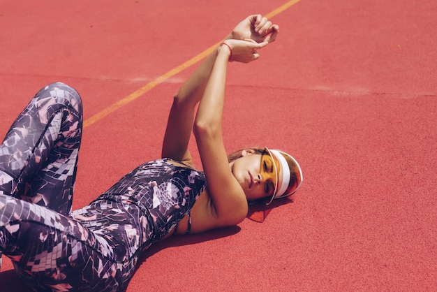 Foto een vrouw in sportkleding ligt op een rode ondergrond en draagt een zonnebril.