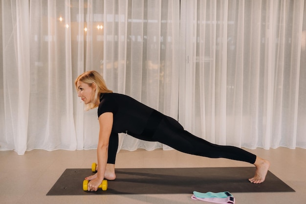 Een vrouw in zwarte sportkleding doet fitness met halters in haar handen Sportgezondheidsgymnastiek en levensstijlconcept