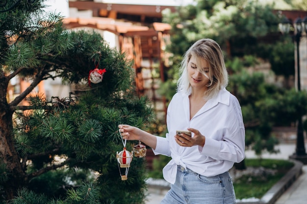 Een vrouw is aan de telefoon en kleedt een kerstboom aan in de tuin van haar huis