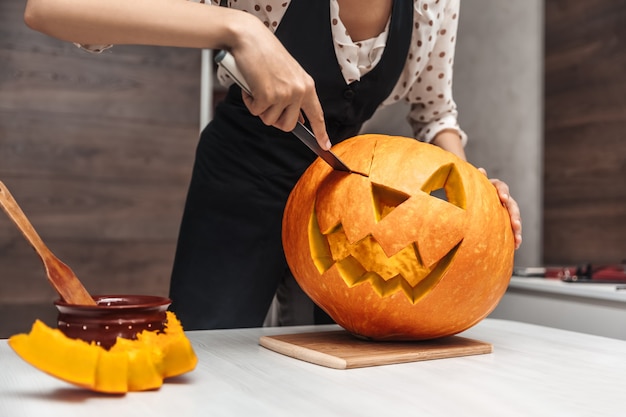 Een vrouw kerft een grote oranje pompoen in een lantaarn voor Halloween