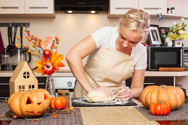 Een vrouw kneedt koekjesdeeg voor Halloween in de keuken met herfstdecor. Gezellig huis en voorbereiding, koekjes maken voor Halloween.