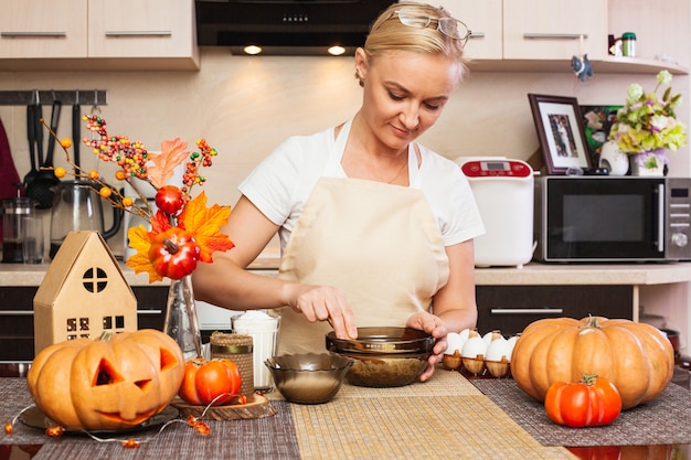 Een vrouw kneedt koekjesdeeg voor Halloween in de keuken met herfstdecor... Gezellig huis en voorbereiding op Halloween. Koekjes maken voor Halloween.