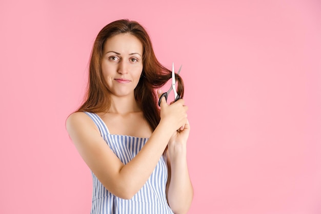 Een vrouw knipt zelf haar lange haar af Studio-opname op een roze achtergrond copyspace