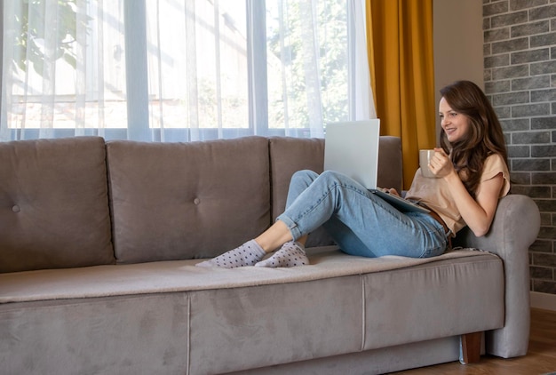 Een vrouw lacht terwijl ze op afstand met iemand praat Een meisje drinkt thee terwijl ze online thuis werkt met een laptop