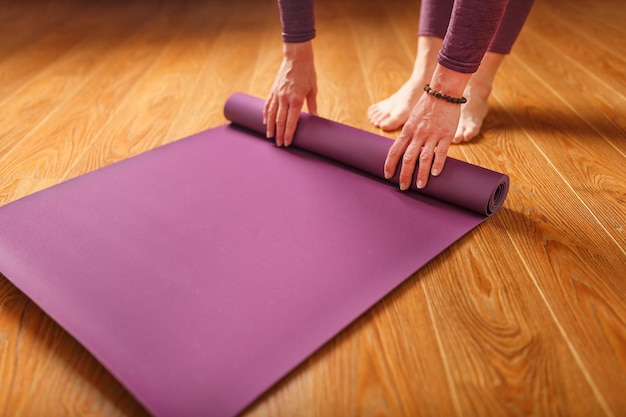 Een vrouw legt een lila yogamat op de houten vloer. Vrouwen die yoga beoefenen. Een gezonde levensstijl in afzondering.