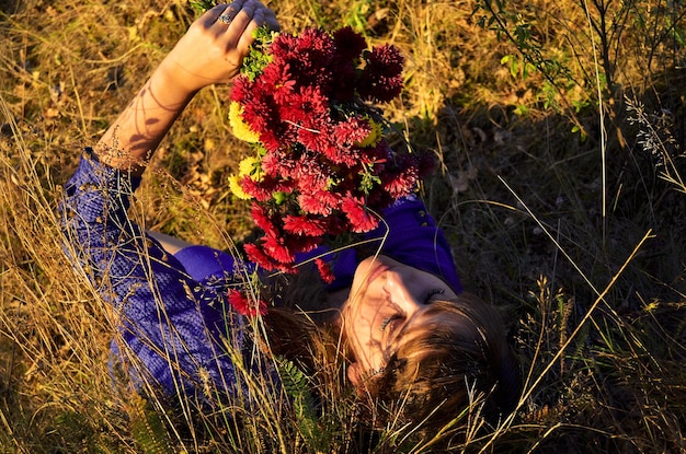 Een vrouw ligt in het gras met een bos bloemen in haar hand.