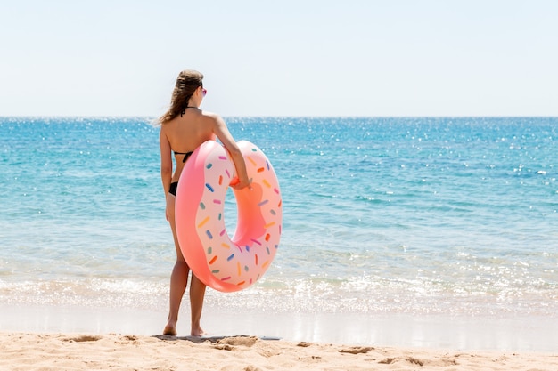 Een vrouw loopt het zeewater in. Meisje ontspannen op opblaasbare ring op het strand. Zomervakantie en vakantie concept.