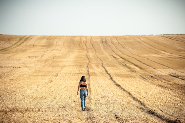 Een vrouw loopt in een veld met bandensporen op de achtergrond.