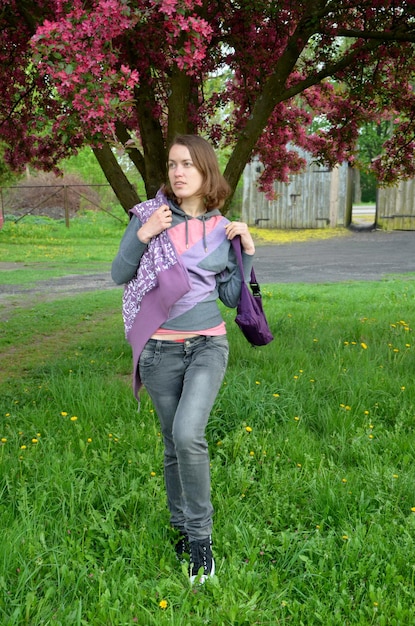 Een vrouw loopt in een veld met bloemen en een boom op de achtergrond.