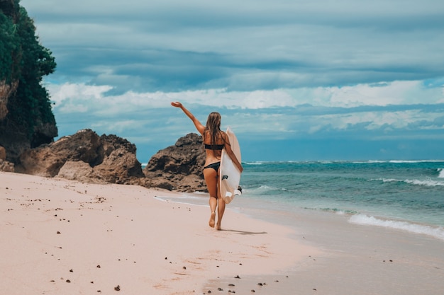 Een vrouw loopt met een surfplank op het strand