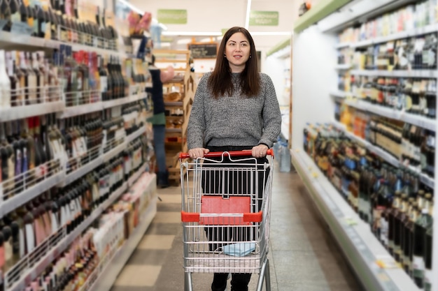 Een vrouw loopt met een winkelwagentje in een supermarkt langs de schappen met boodschappen Winkelen in een grote winkel Productkeuze