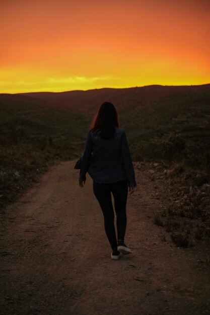 Een vrouw loopt over een onverharde weg naar een zonsondergang