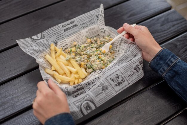 Een vrouw luncht buiten frietjes en salade