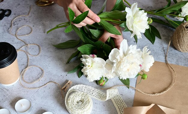 Een vrouw maakt een boeket pioenrozen een boeket kraftpapier bloemen snoeien stylite maakt een boeket