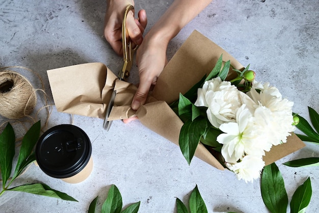 Een vrouw maakt een boeket pioenrozen een boeket kraftpapier bloemen snoeien stylite maakt een boeket