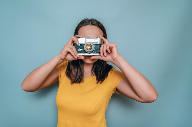 Foto een vrouw maakt foto's met een oude filmcamera gele laarskap zwart haar blauwe achtergrond