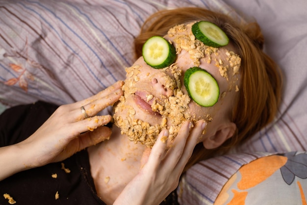 Een vrouw maakt thuis een cosmetisch masker van havermout op haar gezicht en komkommer Anti-aging behandelingen huidverzorgingsconcept