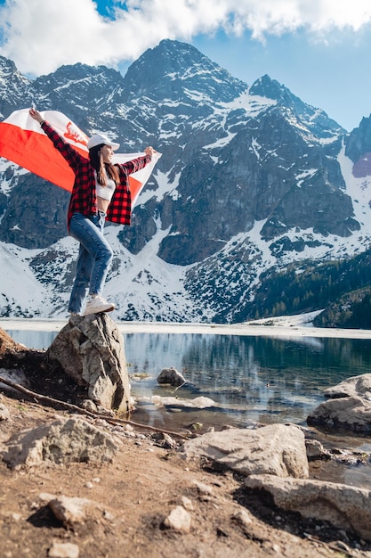 Een vrouw met de vlag van Polen staat aan de oever van een meer Morskie Oko