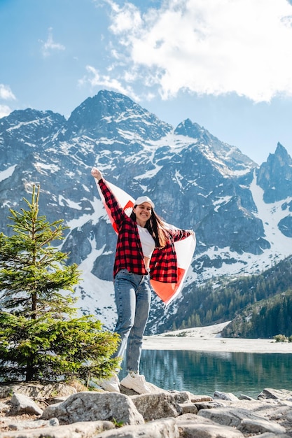 Een vrouw met de vlag van Polen staat aan de oever van een meer Morskie Oko