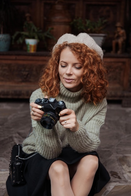 Foto een vrouw met een baret en een groene trui houdt een camera in haar handen en maakt foto's