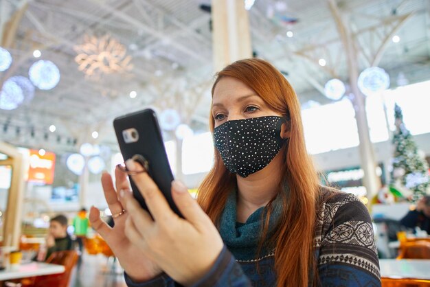 Foto een vrouw met een beschermend masker in een café die sociale afstand in acht neemt met een telefoon in haar hand preventie van coronavirus