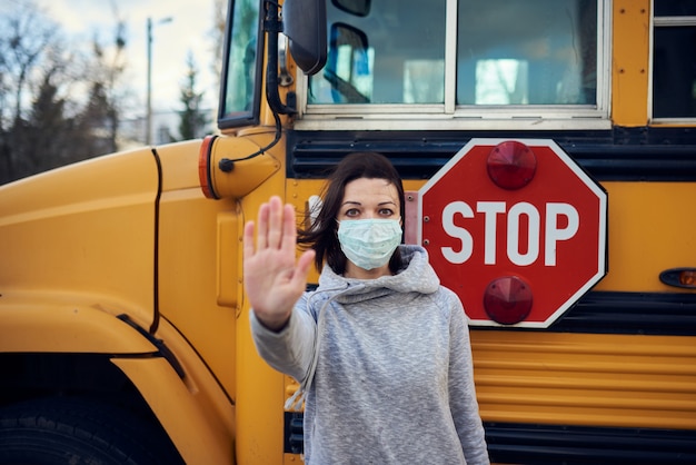 Een vrouw met een beschermend masker staat voor een schoolbus.