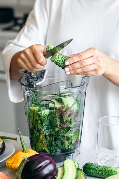 Een vrouw met een blender die komkommer hakken voor een smoothie thuis