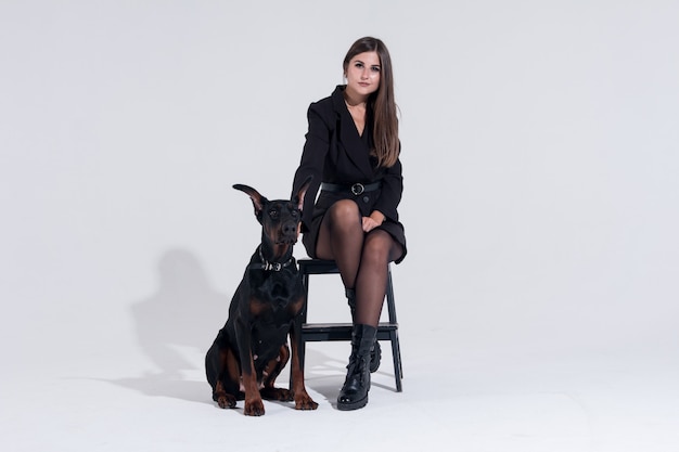 Een vrouw met een doberman zwarte jurk op een witte achtergrond. een vrouw zit op een hoge trap