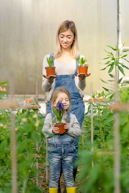 Een vrouw met een dochtertje houdt in het voorjaar potbloemen in een kas.